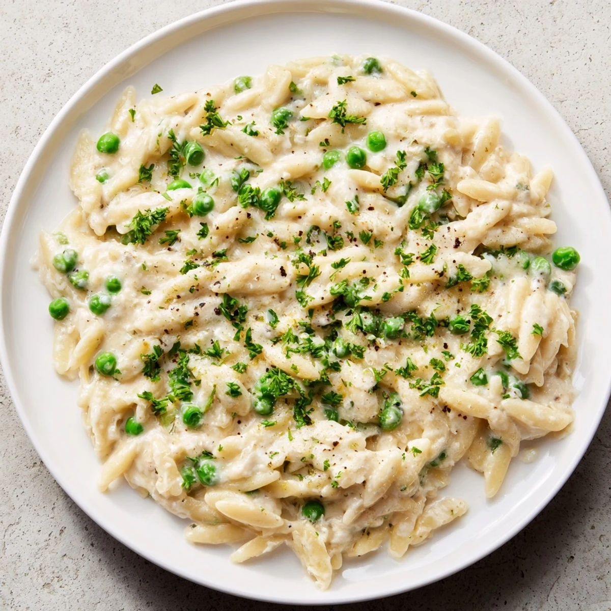 Freshly cooked Creamy Parmesan Orzo with bright green peas, ready to be garnished with parsley.