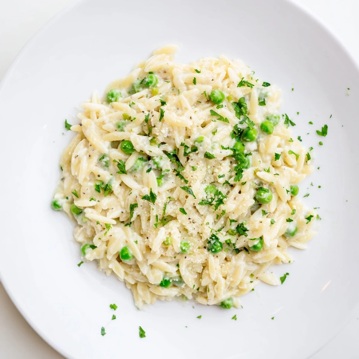 A bowl of delicious Creamy Parmesan Orzo, where orzo pasta and peas rest in a creamy sauce.