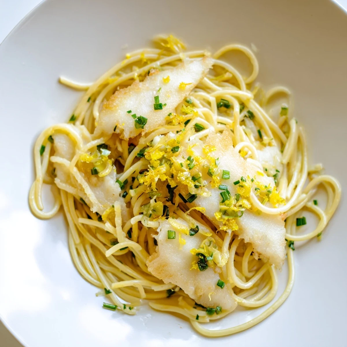 A vibrant bowl of Crispy Fish Pasta featuring golden-brown fish pieces nestled among twirled spaghetti, bright lemon zest, and a drizzle of olive oil.