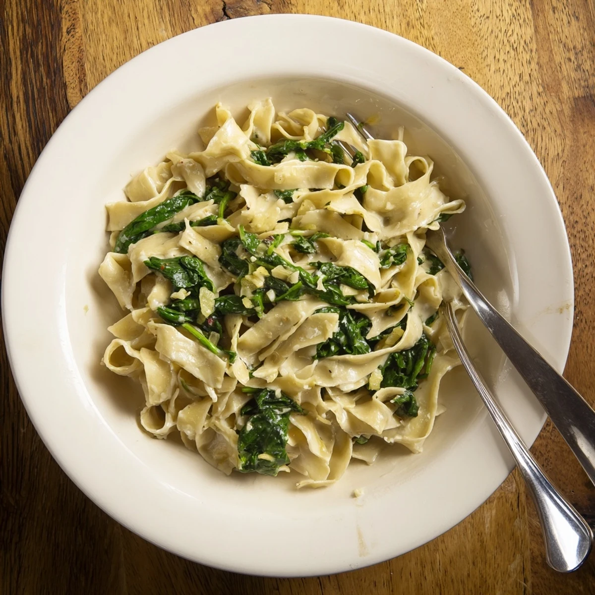 A skillet of Creamy Spinach Garlic Noodles with sautéed onions, spinach, and optional red pepper flakes.