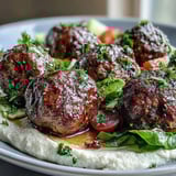 A close-up of spiced venison meatballs, fresh salad, and smooth hummus, arranged artfully on a white plate.