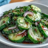 A chilled bowl of Refreshing Crunchy Cucumber Salad topped with sesame seeds, served alongside grilled chicken.