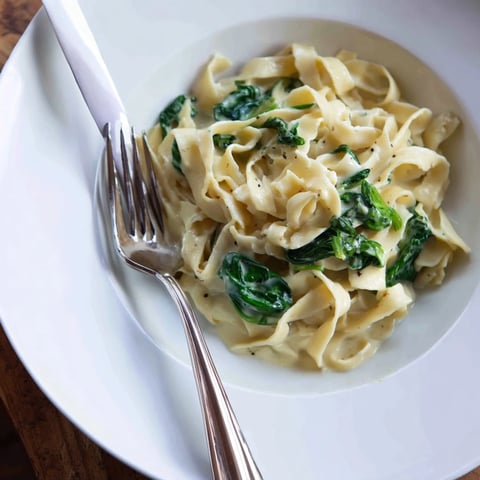 Creamy Spinach Garlic Noodles in a white bowl, fork twirling noodles with wilted spinach and garlic.