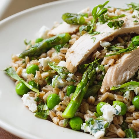Bright, colorful Warm Spring Farro Chicken Salad with grilled chicken slices, blanched asparagus, peas, and crumbled feta on a rustic plate.