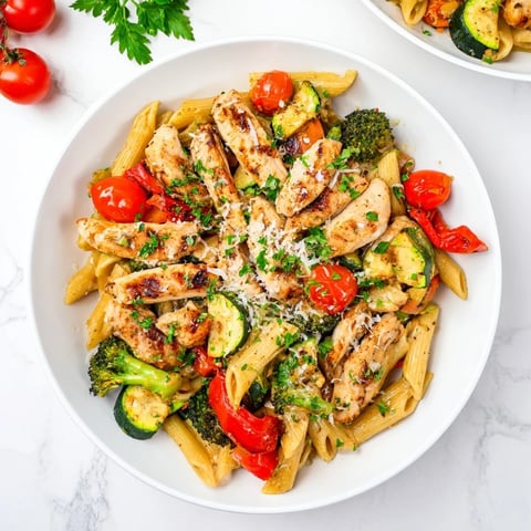 Roasted garlic herb chicken breast slices mingle with colorful bell peppers, zucchini, and cherry tomatoes over penne pasta, garnished with fresh parsley and Parmesan for a satisfying Italian-inspired main dish.