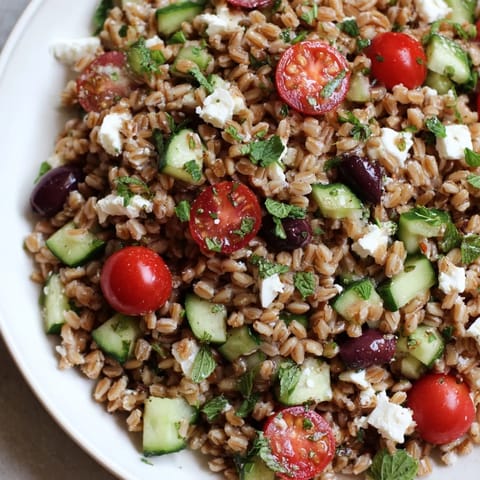 A close-up of the Farro Salad Mediterranean reveals crumbled feta cheese and fresh herbs atop the wholesome grain mixture, perfect for a light lunch or side.  