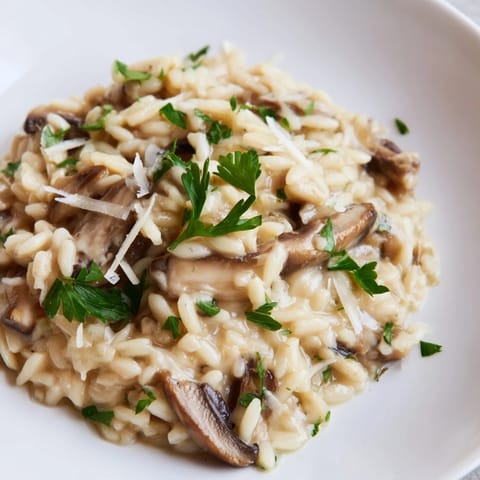A skillet of Orzo Mushroom Risotto-Style with sautéed mushrooms and sweet green peas, served alongside a glass of chilled white wine.
