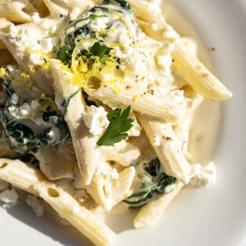 Creamy Feta Spinach Pasta twirled on a fork, showing velvety sauce, wilted spinach, and crumbled feta against a rustic background.