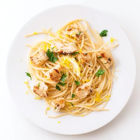 A close-up of Brown Butter Lemon Chicken Pasta in a skillet, showcasing glistening noodles, tender seared chicken, and melted Parmesan cheese.