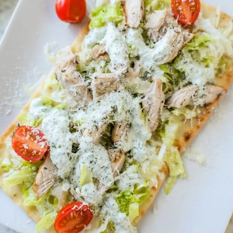 Golden Caesar Chicken Flatbread topped with fresh romaine, grated Parmesan, and juicy sliced chicken on a baking sheet.