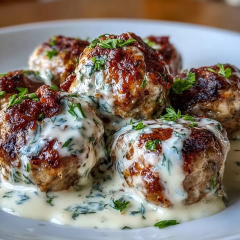 Four savory Creamy Garlic Ranch Turkey Meatballs rest in a rich, creamy sauce, paired with mashed potatoes on a rustic plate.