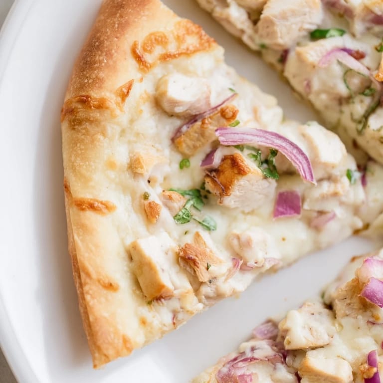 A freshly baked Chicken Alfredo Pizza sits on a wooden board, garnished with parsley and ready to serve.