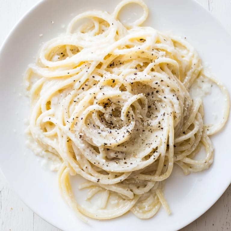 Tossed Spaghetti Cacio e Pepe in a warm skillet, creating a creamy, velvety sauce perfect for a quick Italian dinner.