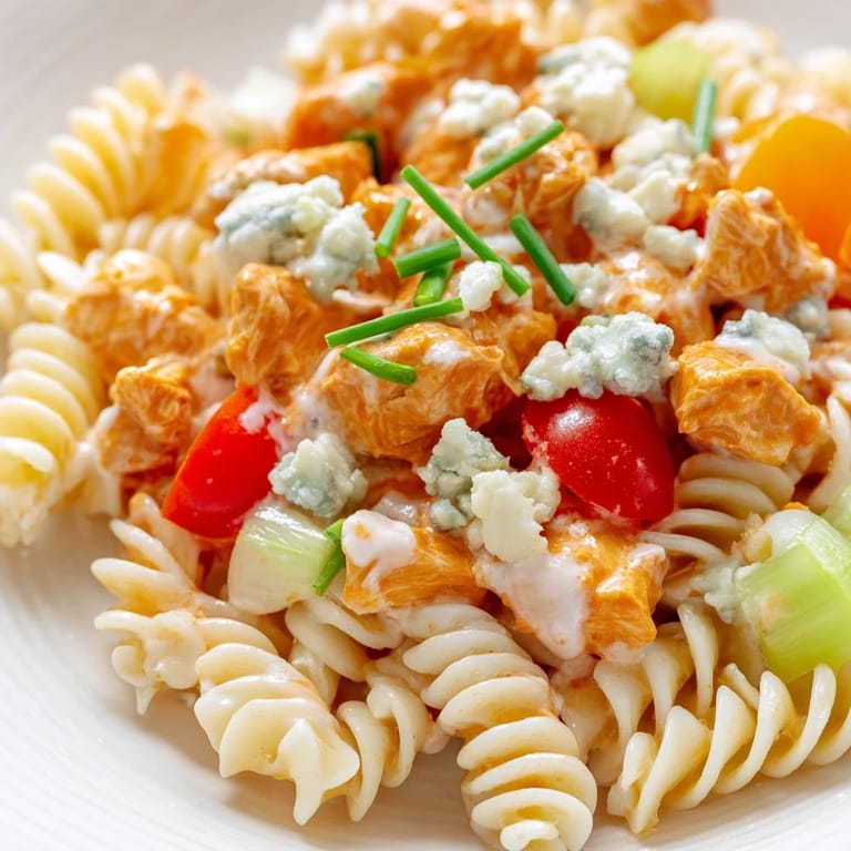 Rotini pasta tossed with spicy buffalo chicken, diced red bell pepper, and fresh chives for a potluck side.