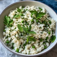 Spring Pea and Mint Rice Pilaf in a white bowl, garnished with fresh mint leaves and lemon wedges, perfect for Easter dinner or spring gatherings.
